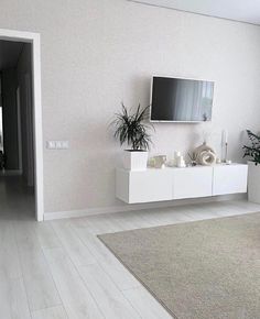 a living room with white furniture and a flat screen tv mounted on the wall above it