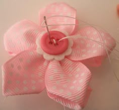 a pink flower with white polka dots and a button on the center is being sewn