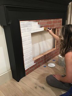 a woman painting a brick fireplace with white paint on the mantle and wood flooring