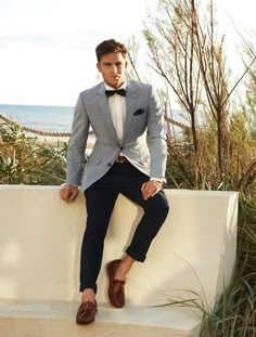 a man in a suit and bow tie sitting on a wall next to the ocean