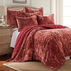 a bed with red comforter and pillows in a room next to a dresser,