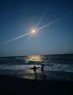 two people are standing on the beach at night with their arms spread out in front of them