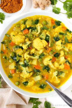 a white bowl filled with vegetable soup next to two bowls of spices and spoons