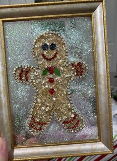 a hand holding up a frame with an image of a gingerbread man made out of sequins