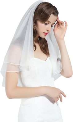 a woman wearing a white veil and holding her hand up to her face while she wears a wedding dress