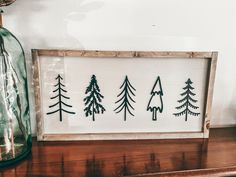 a wooden sign with three trees on it sitting on top of a shelf next to a glass bottle