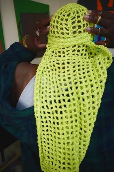 a woman wearing a yellow knitted shawl with her hands on the back of her head