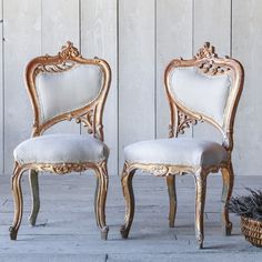 two white chairs sitting next to each other in front of a wooden wall and basket