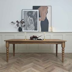 a wooden table with two candles on it in front of a painting and vases