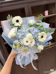 a bouquet of white and blue flowers is being held up by someone's hand