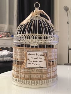 a white birdcage with a sign on it's side sitting on a table