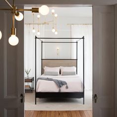 an open door leading to a bedroom with a four poster bed and white walls, along with wooden flooring