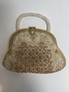 "This is really a lovely Spectacular Small vintage beaded bag. Its previous owner told me it was from 1960s. It's beaded gold and white beads, some of the beads in the center are in a beige tone.  It's in excellent condition no stains to front or back or handle, but I do see a stain inside, please see photos. I think it might be able to be removed. I'm not sure about that. Also includes a small mirror inside. Measures 7\" at the bottom and tapers upward to 5 1/4\"" Gold Vintage Bags, Vintage Embellished Bag For Festive Occasions, Vintage Embellished Bags For Festive Occasions, Vintage Handwork Evening Bag For Wedding, Handmade Vintage Evening Bag For Festive Occasions, Vintage Handmade Evening Bag For Festive Occasions, Gold Beaded Evening Bag For Wedding, Vintage Bags For Festivals, Traditional Gold Evening Bag With Pearl Embroidery