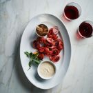 a white plate topped with meat and veggies next to two glasses of wine