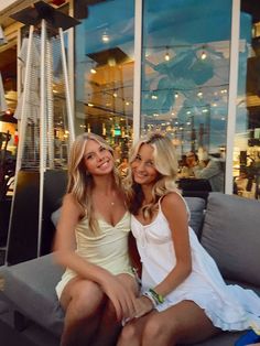 two beautiful young women sitting next to each other on a couch in front of a building