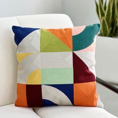 a colorful pillow sitting on top of a white couch next to a potted plant