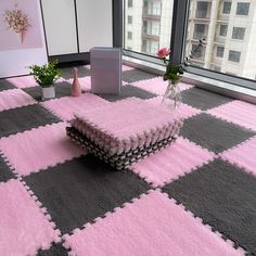 a pink and gray carpet with squares on it in front of a window, vases filled with flowers