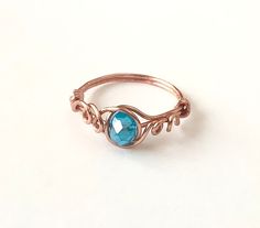 a gold ring with a blue stone in the center and vines around it, on a white surface