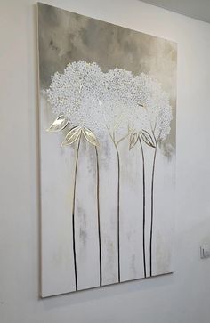 a painting hanging on the wall next to a white vase with flowers and leaves in it