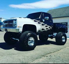 a white truck with flames painted on it's hood and tires is parked in front of a garage