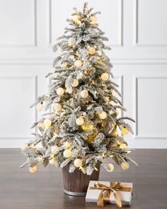 a white christmas tree with yellow balls on it and a gift box in the foreground