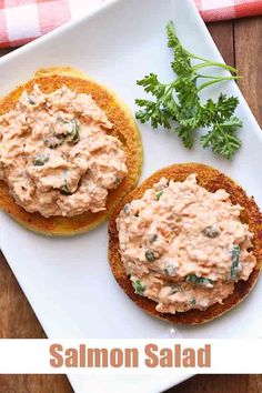 two small sandwiches with salmon salad on them are sitting on a white plate next to a red and white checkered napkin