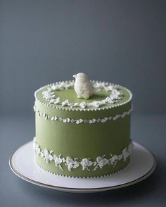 a green cake with white frosting and a small bird on top, sitting on a plate