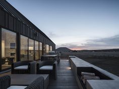 an outdoor seating area on the side of a building with large glass windows at dusk