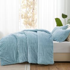 a bed with two pillows and a blanket on it in front of a white window