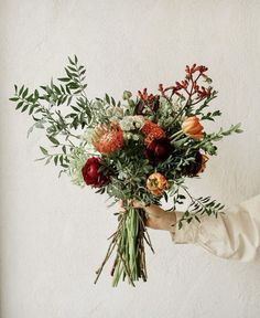 a person holding a bunch of flowers in their hand with greenery on the side