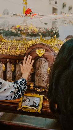 a person reaching up to the top of a wooden casket with gold decorations on it