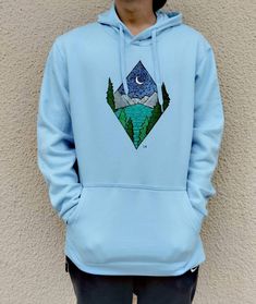 Men’s hoodie with minimal geometric landscape design in the chest area. The design is handpainted and it represents a lake scene with mountains in the background during night time. It’s created in an abstract kind of way and it’s painted with a natural palette of colors. It’s a great gift idea for your loved ones (especially for those who love nature) or for yourself. The hoodie despite the baby blue color shown in the photos, is also available in black. The size scale contains S, M, L and XL.
The hoodie itself has a front pocket and a back hood with strings that fall in the front. It’s made out of cotton and polyester so it’s breathable and comfortable. Blue Hoodie With Screen Print, Blue Sweatshirt With Kangaroo Pocket For Outdoors, Blue Sweatshirt With Kangaroo Pocket For Outdoor Activities, Blue Hoodie With Kangaroo Pocket For Outdoor Activities, Blue Cotton Hoodie For Outdoor Activities, Blue Sweatshirt With Adjustable Hood For Outdoor, Blue Adjustable Hood Sweatshirt For Outdoor, Geometric Landscape Design, Geometric Landscape