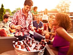 a group of people sitting around a table filled with bottles of beer and smiling at each other