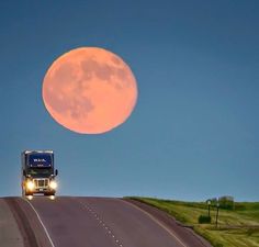 a semi truck driving down the road in front of a full moon on a clear day