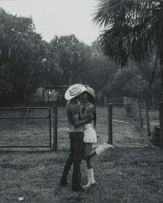 a man and woman kissing in the rain under an umbrella, with trees behind them