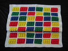 a crocheted blanket with multicolored squares and dots on the bottom, sitting on a black surface