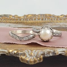 Timeless and classic, this vintage inspired pearl engagement ring and curved wedding band set are reminiscent of the Edwardian era when fine metalwork was designed with intricate details and delicate settings that were fashioned to resemble the patterns of fine lace. The vintage style Edwardian-inspired pearl ring is handcrafted from recycled sterling silver where a lightly oxidized floral band is set with a luminous 8-8.5mm cultured creamy white freshwater pearl in a filigree heart-crown settin Elegant Wedding Jewelry With Milgrain Detail, Classic Pearl Ring For Wedding, Classic Wedding Pearl Ring, White Gold Pearl Ring For Wedding, Milgrain Round Cut Wedding Ring, Engraved White Gold Stackable Rings For Wedding, Engraved Stackable Rings In White Gold For Wedding, Elegant Milgrain Jewelry For Wedding, Elegant Milgrain Wedding Jewelry