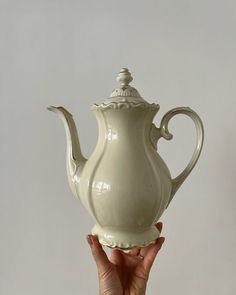 a hand holding a white ceramic tea pot