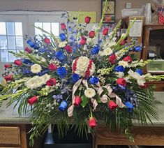 an arrangement of red, white and blue flowers in a vase on a counter top