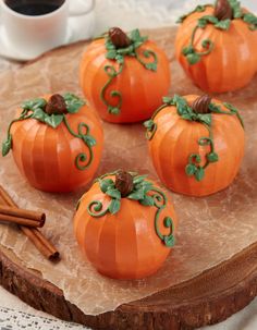 small pumpkins decorated with green leaves and cinnamon sticks on a wooden board next to a cup of coffee