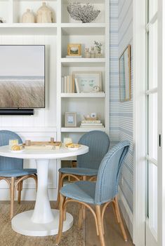 two blue chairs sit at a white table in front of a book shelf with books on it