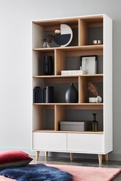 a white bookcase with wooden shelves filled with books and vases on top of it