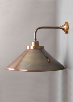 an industrial style wall light with a brass finish on the arm and metal cone shade