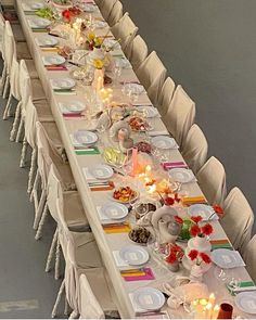 a long table is set up with white chairs and place settings for the dinner party