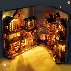 an open book with miniature houses lit up in the dark and flowers on the ground