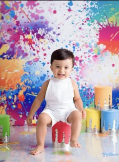 a baby sitting on top of a wooden block in front of paint splatters