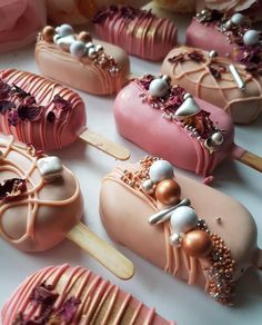 there are many pink and gold decorated desserts on the table with wooden skewers