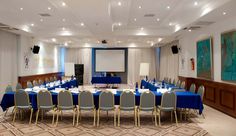 a large conference room set up with blue and white linens, gold chairs, and a projector screen