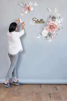 a woman standing in front of a wall with flowers and the word stella on it