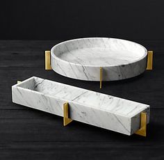 two white marble trays with gold handles on a black surface, one is round and the other is rectangular